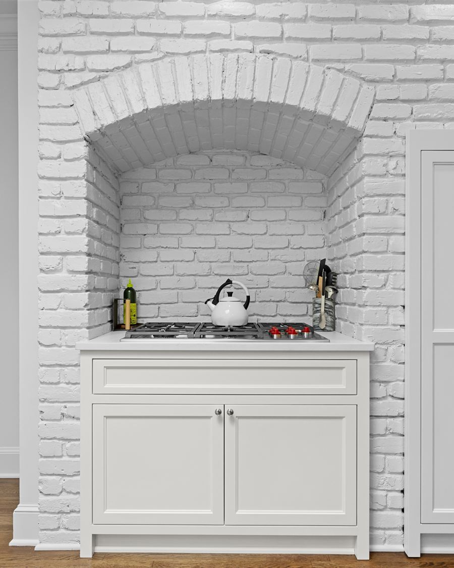 The same brick alcove after renovation by Revival Construction, painted white with a custom range cabinet and cooktop set into the arch
