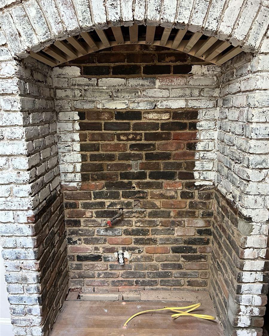 Original brick range alcove in a historic Charlotte kitchen before renovation, with exposed brick, a bare arch and rough-in plumbing
