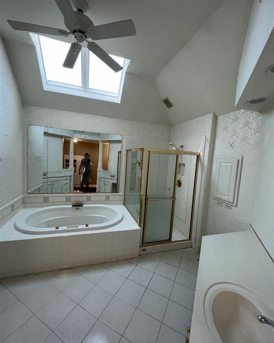 Dated 1990s primary bathroom with jetted tub deck, brass-framed shower and wallpaper, before renovation