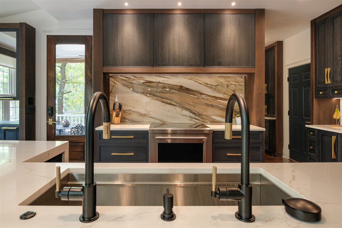 Stainless sink with two matte black faucets facing a jumbo porcelain slab backsplash, Charlotte chef's kitchen remodel