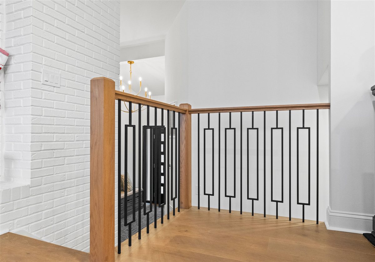Stair landing with an oak rail and black geometric balusters, River Chase renovation