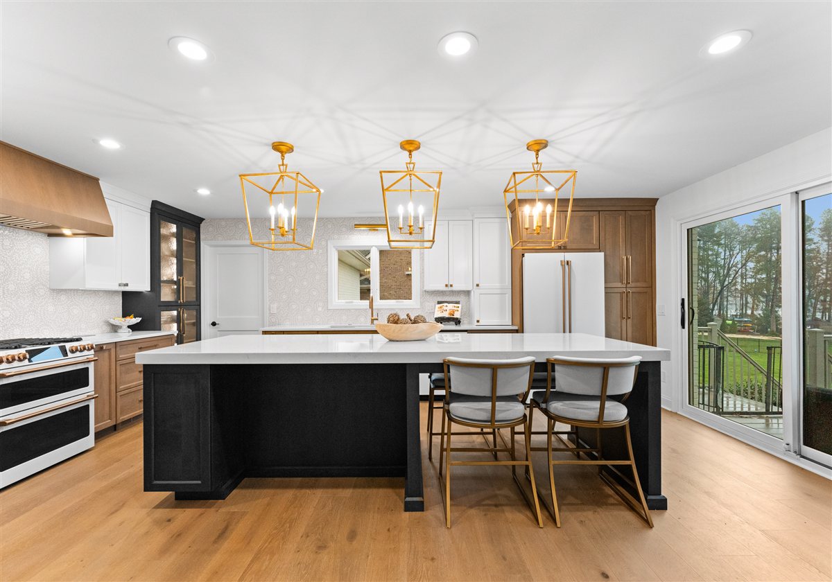 Dark kitchen island with seating under brass lantern pendants, River Chase renovation