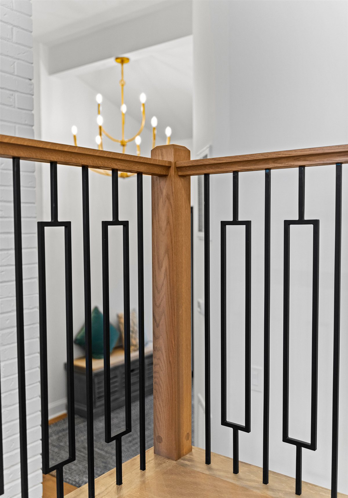 Oak and iron stair railing with a brass chandelier above, River Chase renovation