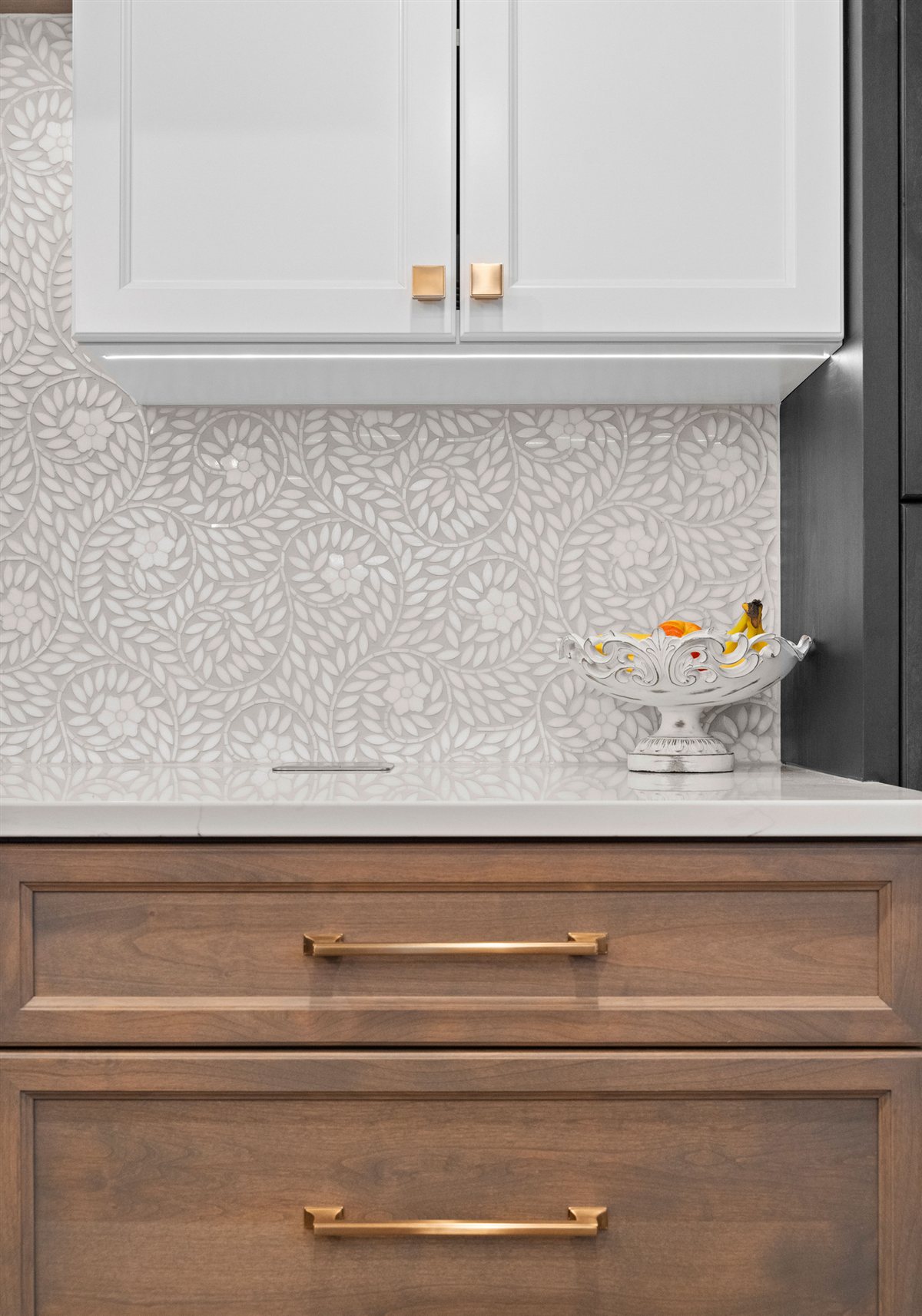 Wood drawers with brass pulls under a patterned tile backsplash, River Chase kitchen
