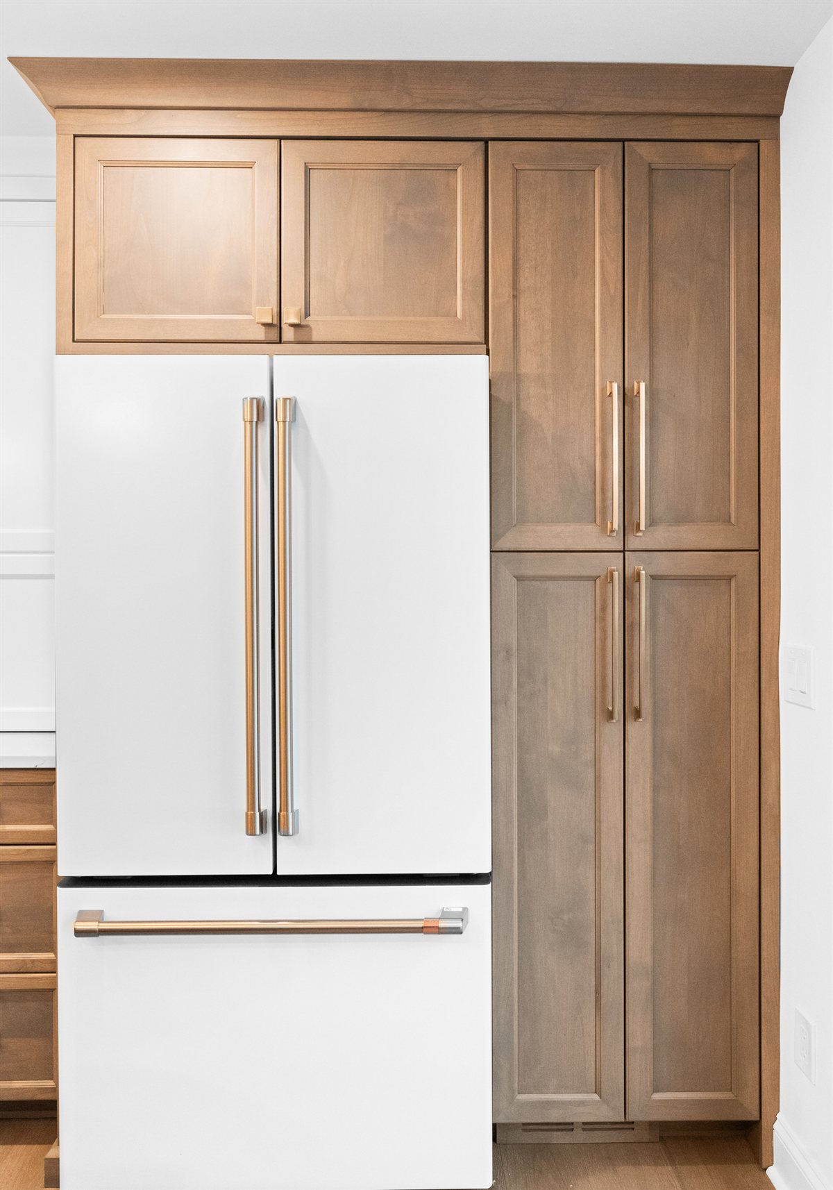 White refrigerator beside tall wood pantry cabinets, River Chase kitchen