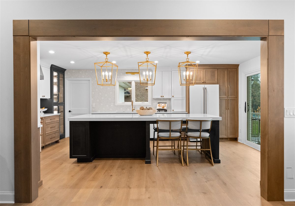 Kitchen and dark island seen through a wood-cased opening, River Chase renovation