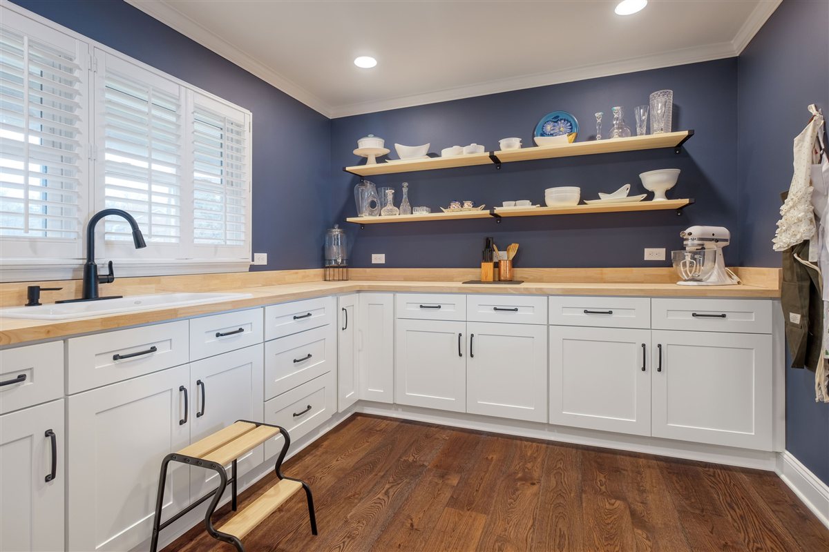 White cabinetry with floating wood shelves against a blue wall, Moss Lake kitchen