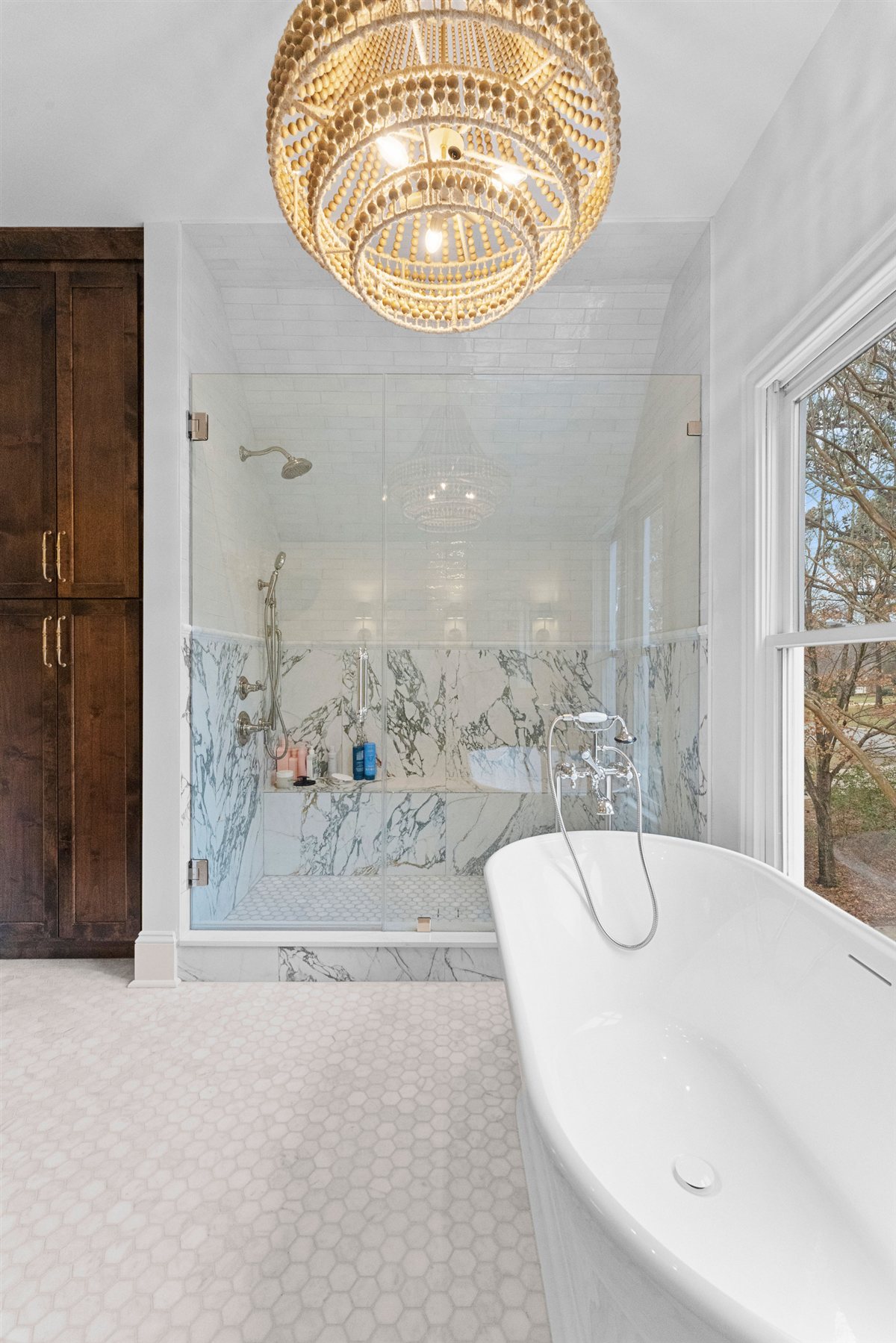 Freestanding tub and gold chandelier beside a dark wood cabinet, The Point renovation