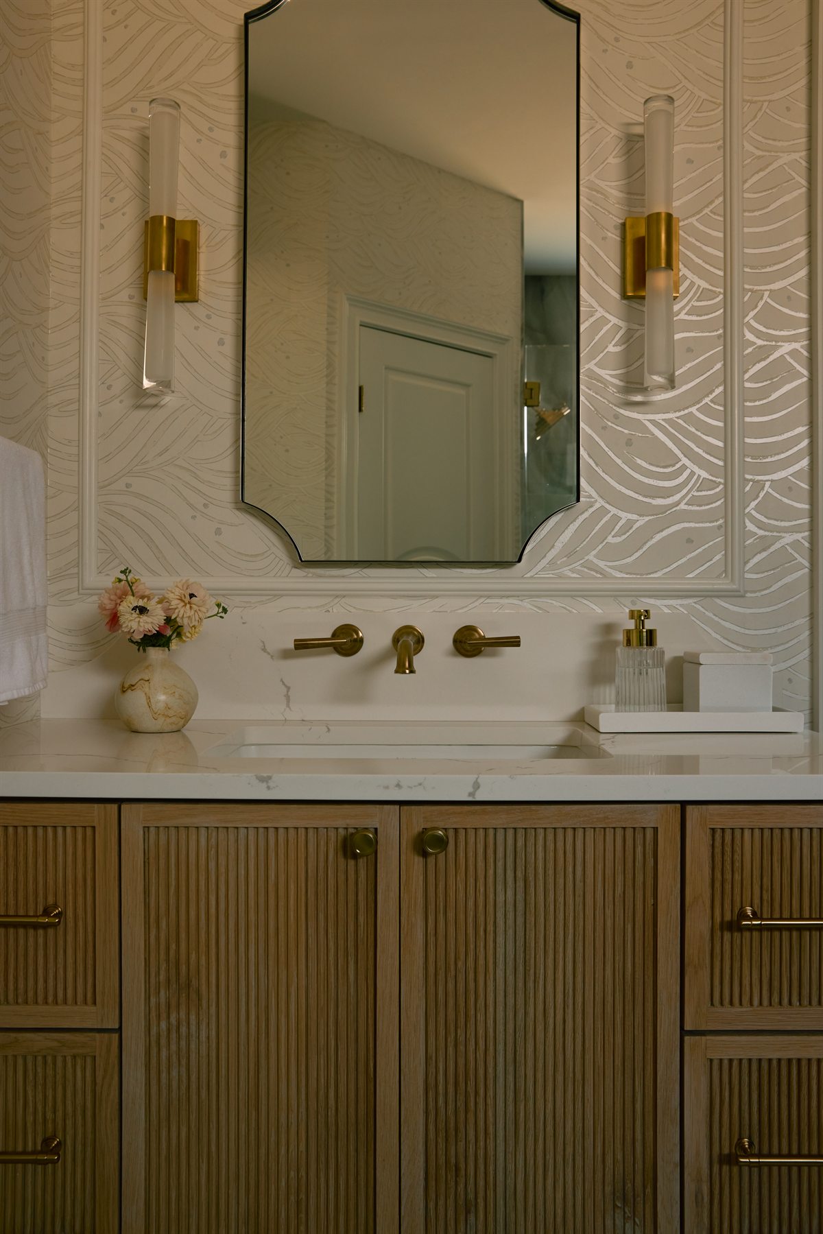 Fluted wood vanity with a brass wall-mount faucet, scalloped mirror and brass sconces, Charlotte primary bath remodel