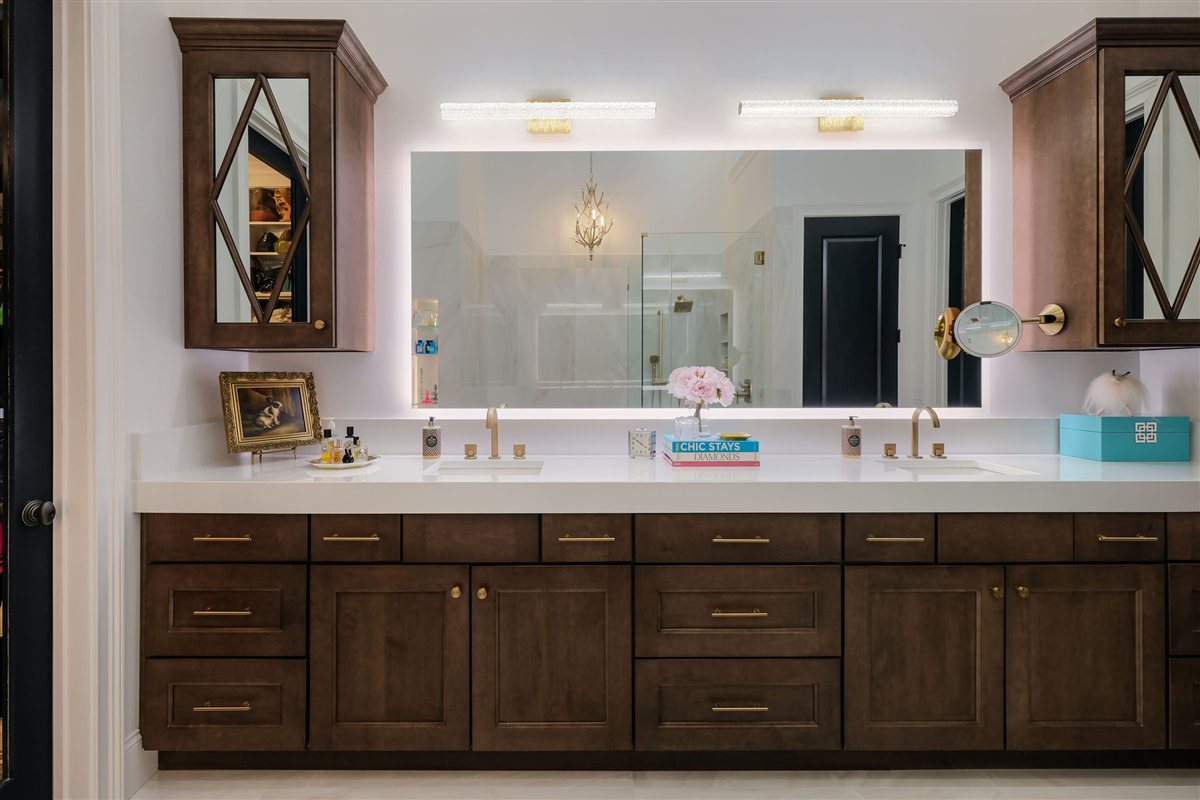 Dark wood vanity with a backlit mirror and brass faucets, Uptown primary suite