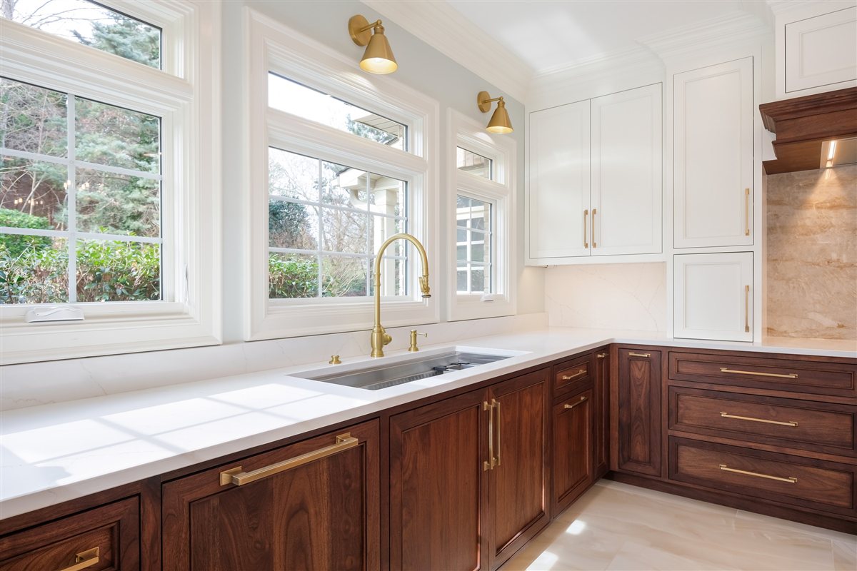 Sink under windows with walnut cabinets and brass faucet, Waxhaw kitchen