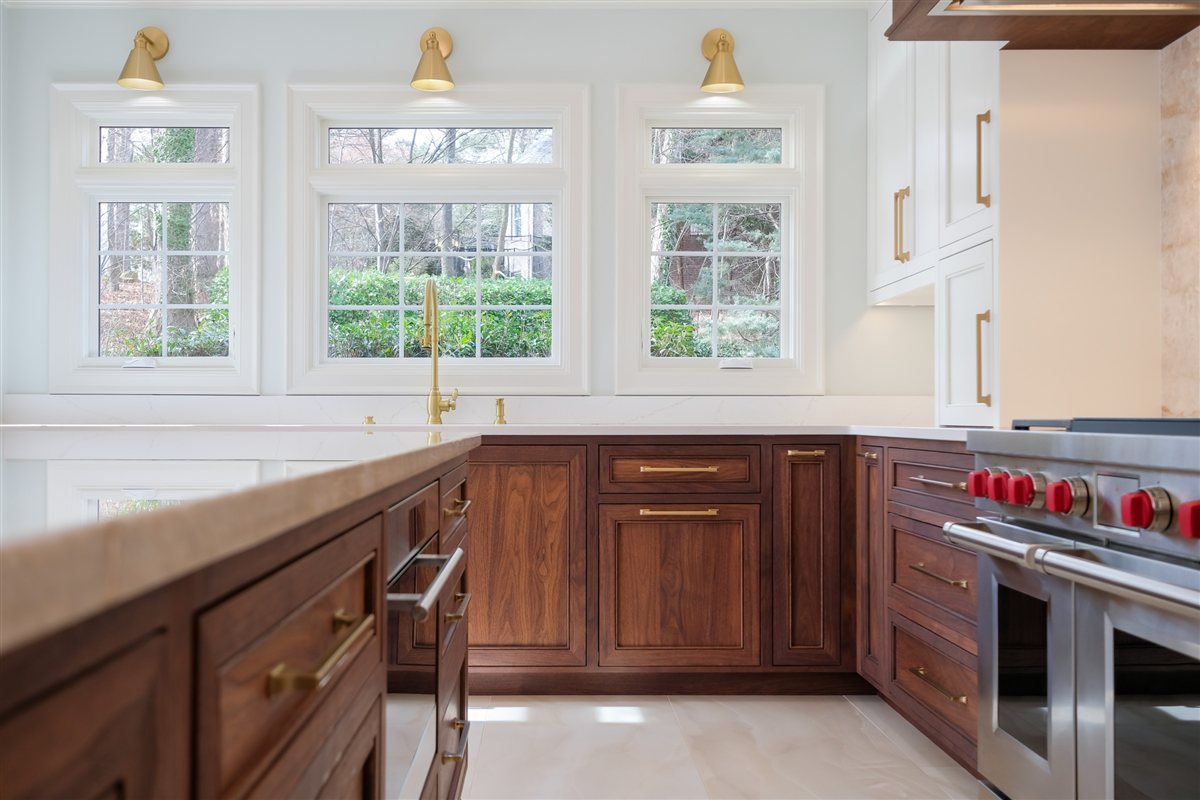 Walnut cabinets and red-knob range beneath windows, Waxhaw kitchen